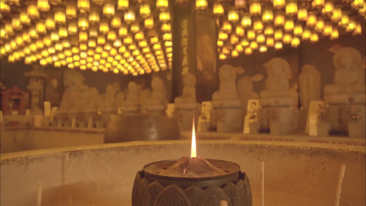 A panoramic view of a serene temple hall on Miyajima Island, Japan, glowing with lantern light and rows of Buddha statues.