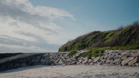 Felshang-Bedeckt-Mit-Grün,-Der-Zu-Einem-Sandstrand-Unter-Einem-Blauen-Himmel-Mit-Wolken-In-Ovar,-Portugal-Führt