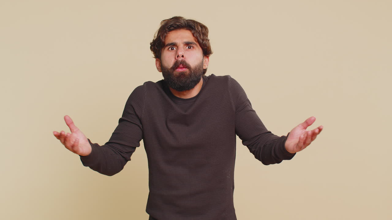 Confused man raising hands asking reason of failure demonstrating disbelief on beige background