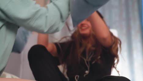 young girl with long hair covering her face smiles while playfully engaging in pillow fight indoors, her joyful expression and energetic posture capture fun childhood moment