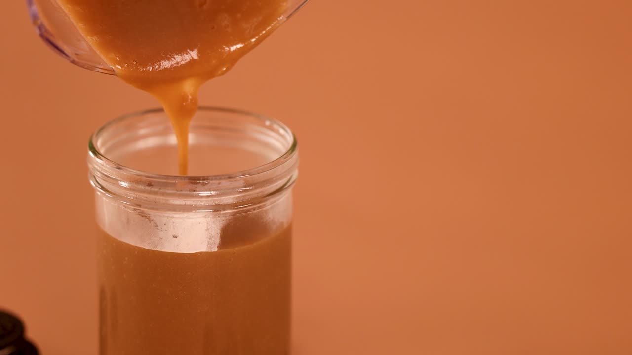 Thick chocolate milkshake smoothly pours into clear glass jar, warm lighting, static camera, macro view