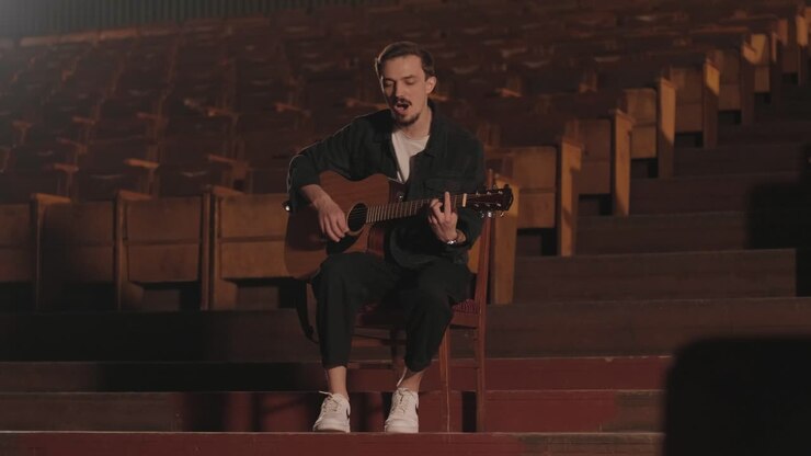 Un bel ragazzo suona una chitarra acustica in un cinema abbandonato. Il musicista canta una canzone e si accompagna con la chitarra