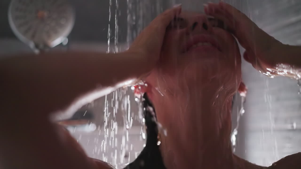 la mujer se relaja en los aerosoles de agua de la ducha de cerca. la dama bonita con los ojos cerrados y el cabello mojado disfruta de los aerosoles refrescantes en el baño. procedimientos de cuidado de spa