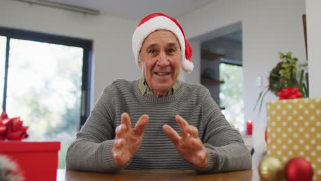 Happy-caucasian-senior-man-wearing-santa-hat-making-video-call-at-home,-talking