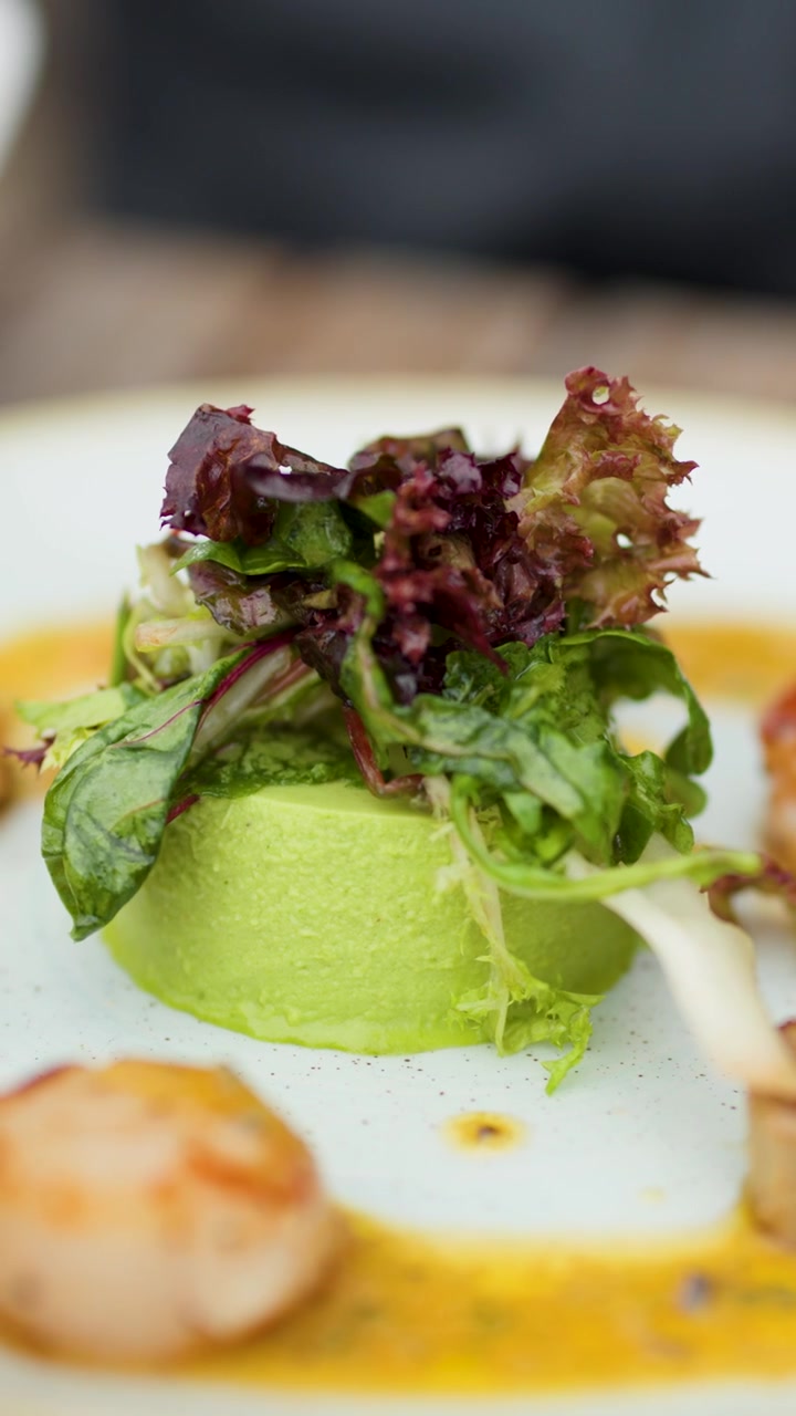 Kameraet sirkler sakte rundt gourmet panna cotta med grønne erter, kamskjell og salat i naturlig dagslys
