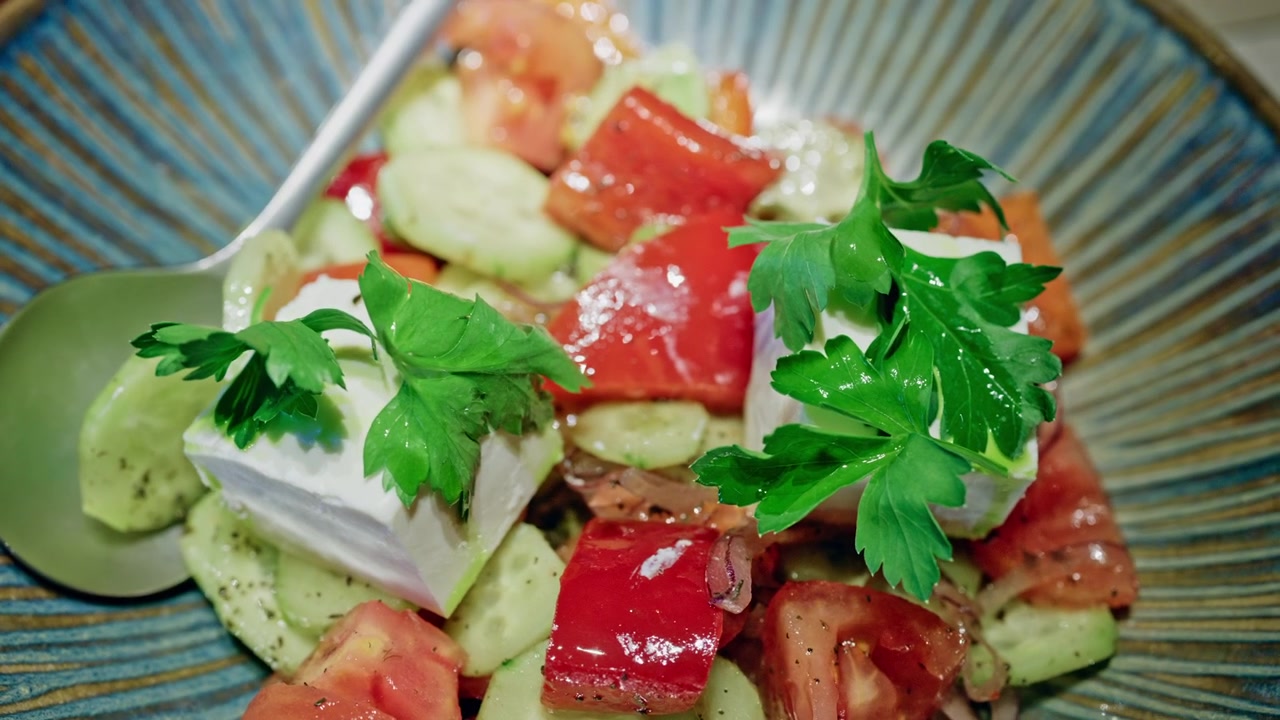 Nærbillede af en middelhavsinspireret salat med friske agurkeskiver, modne tomatstykker, rødløg og tern af fetaost, toppet med persilleblade