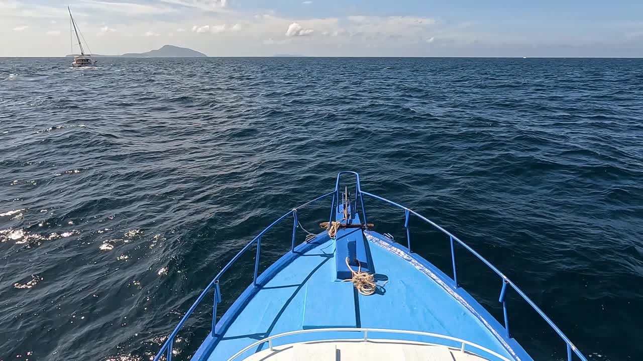A boat travels through the ocean near Phuket, Thailand, under clear skies with gentle waves and bright sunlight