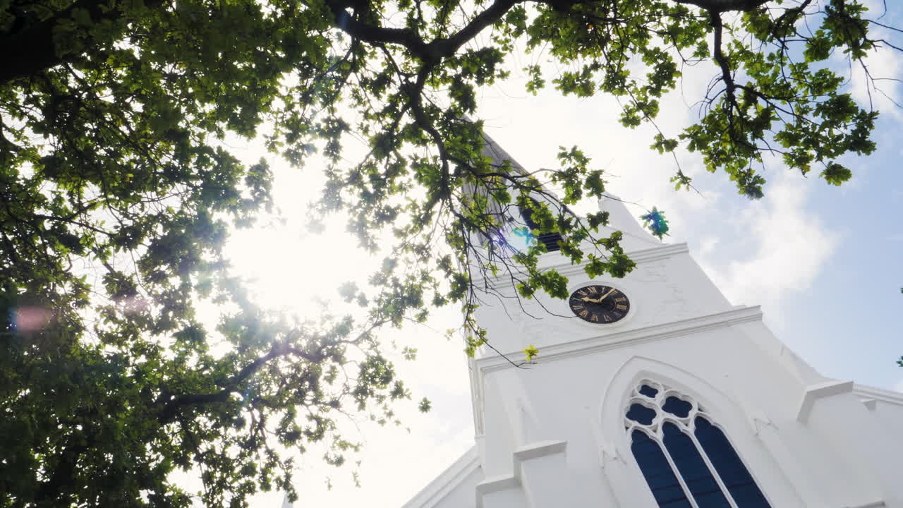 Heavenly white church in South Africa, sun shining through leaves as the church's tower is revealed