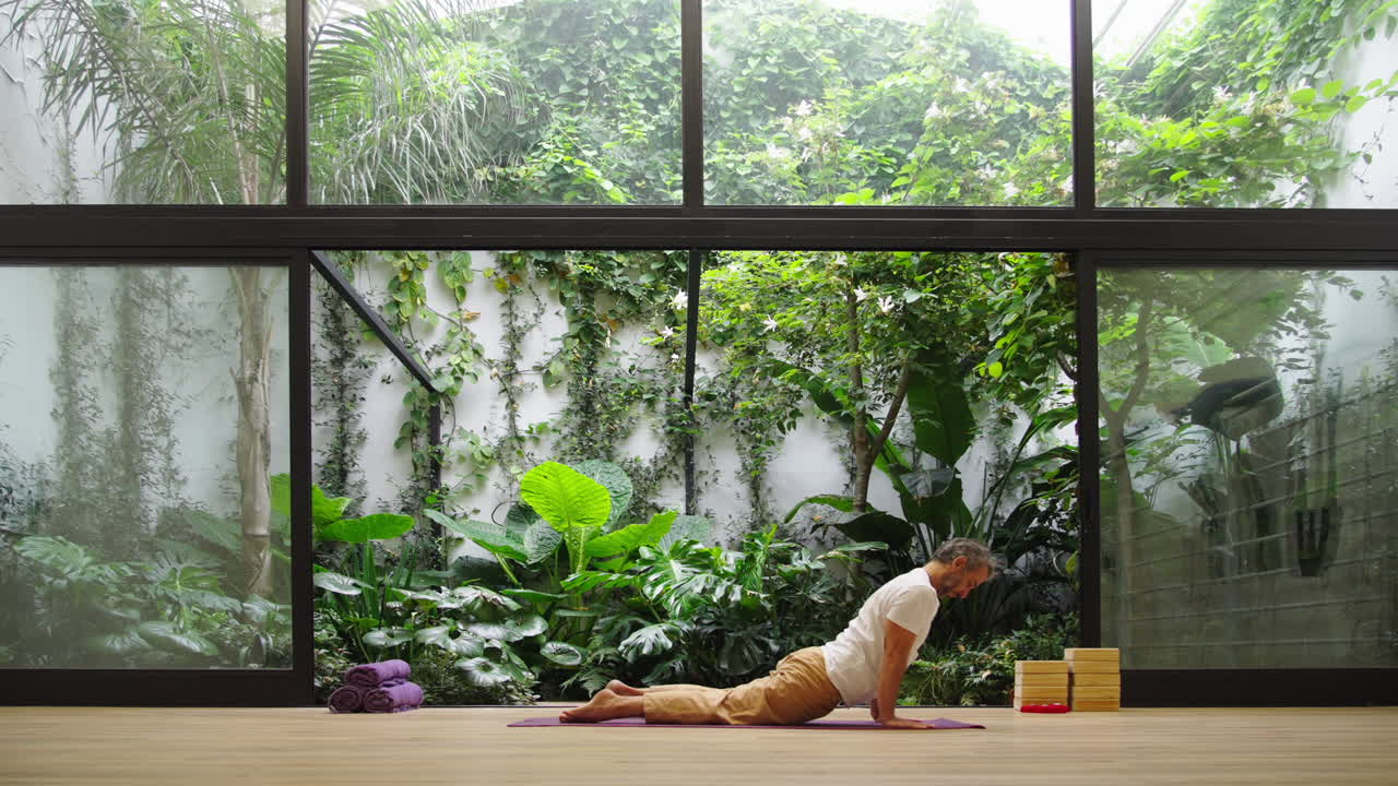 Uomo che pratica la posa yoga del Cobra in un sereno studio con giardino interno