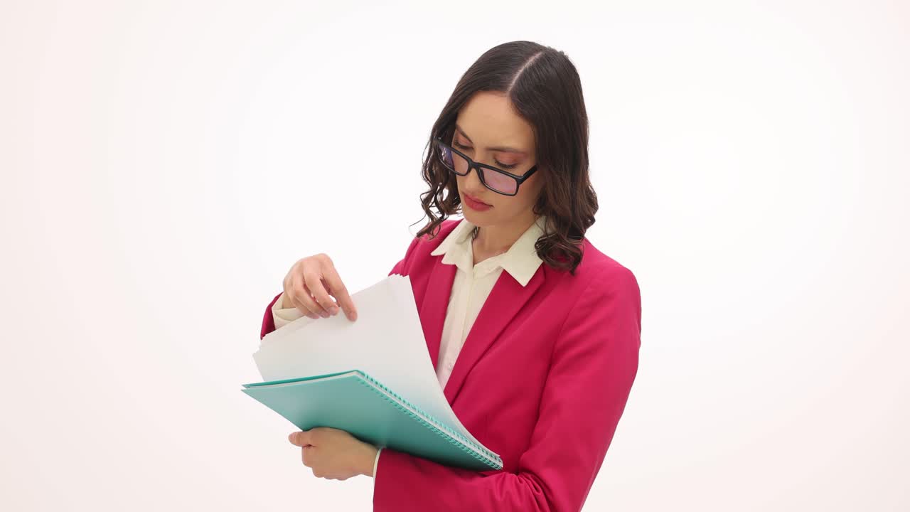 A woman in a pink blazer and glasses reviews documents in a binder