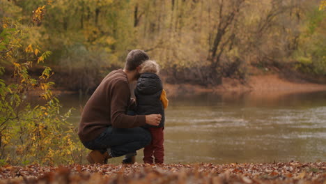caucasian father and little son are resting at shore of forest pond at autumn enjoying nature and warm weather at fall spending time together
