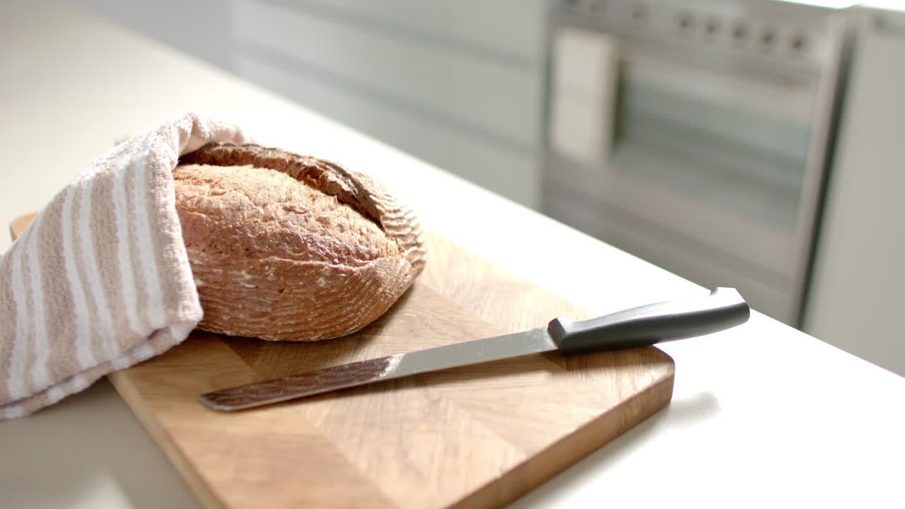 Freshly baked bread resting on wooden cutting board with a knife beside it