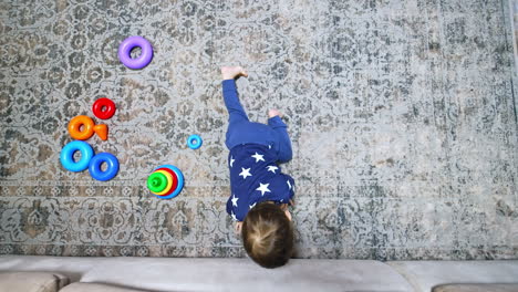 little baby crawling by the carpet. kid reaches his hand under the sofa and pulls the phone out. child playing with gadget. top view.