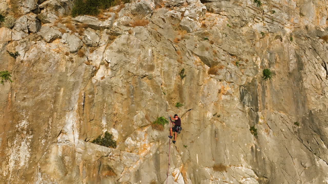 Aerial view away from a man rope climbing a steep mountain wall, golden hour