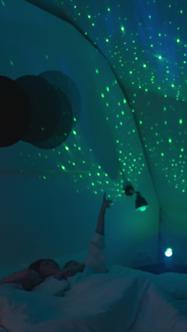 엄마는 천장에 손가락을 가리키며 눈 색 담요로 침대에 누워있는 아이에게 별을 보여줍니다. 편안한 분위기에서 잠자리에 들기 전에 엔터테인먼트와 휴식을 취합니다.