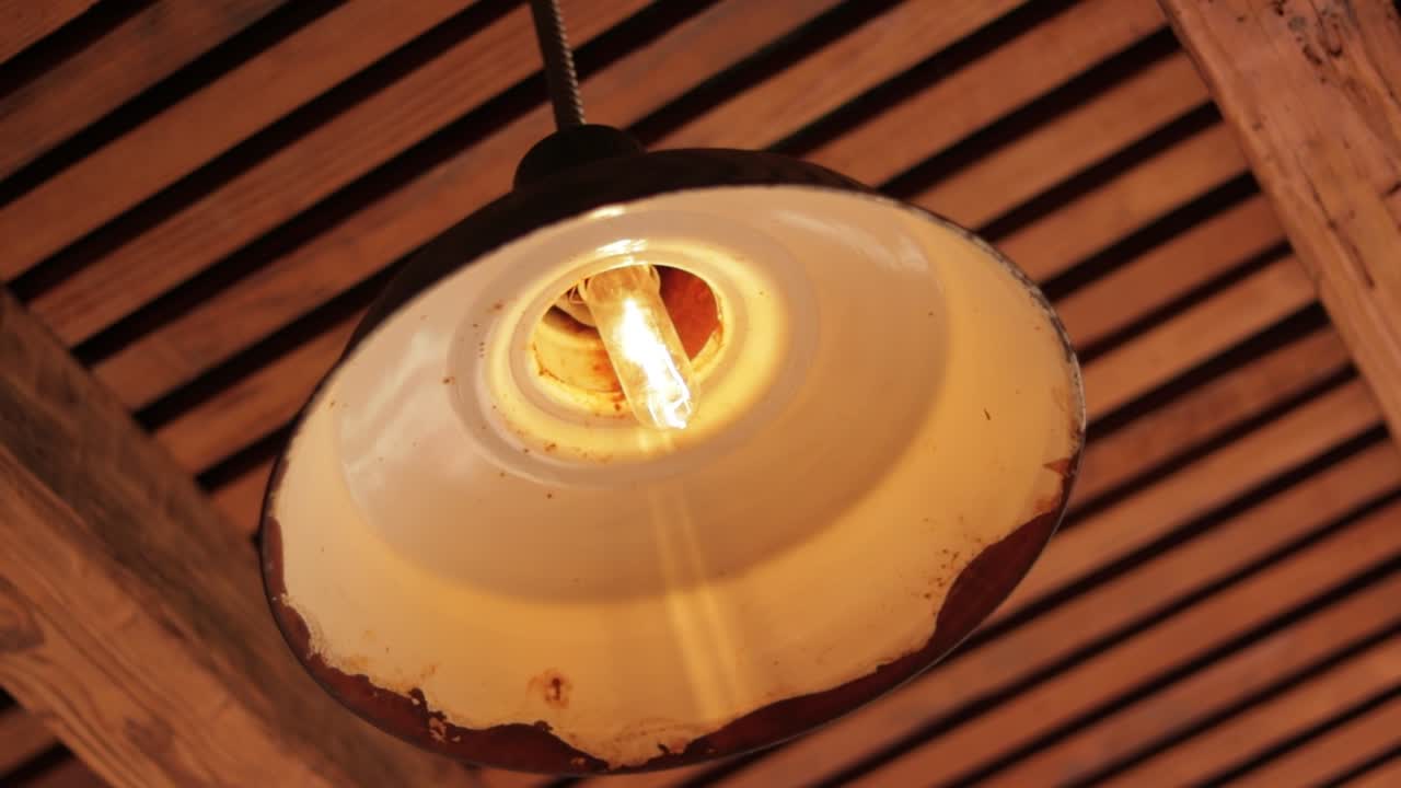 Rusty crude lamp with warm light hanging from wooden plank ceiling