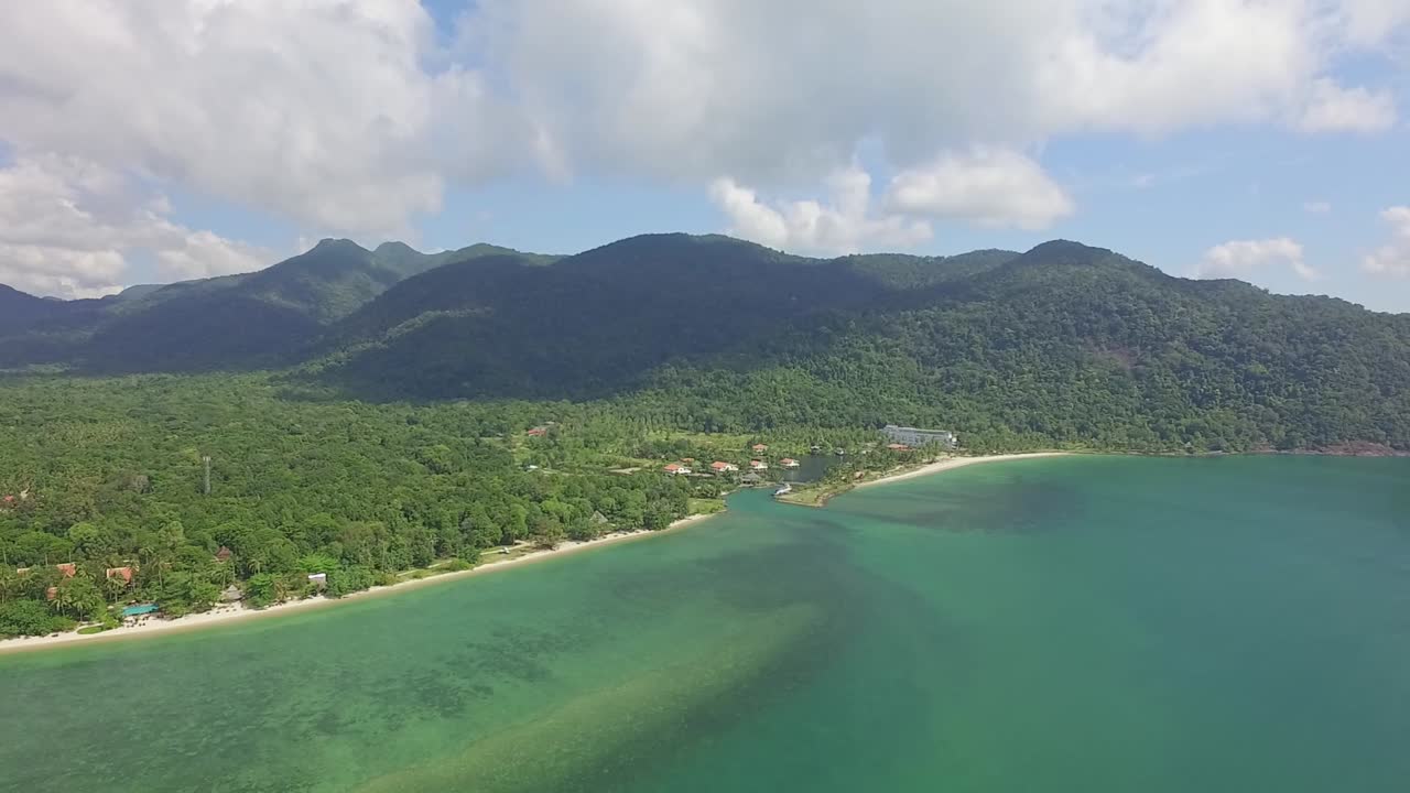 Aerial back tracking shot of a tropical beach on Koh Chang showing mountains with lush dense Jungle and a sea view