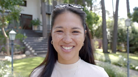 Happy-asian-woman-with-sunglasses-standing-and-smiling-in-sunny-garden,-slow-motion