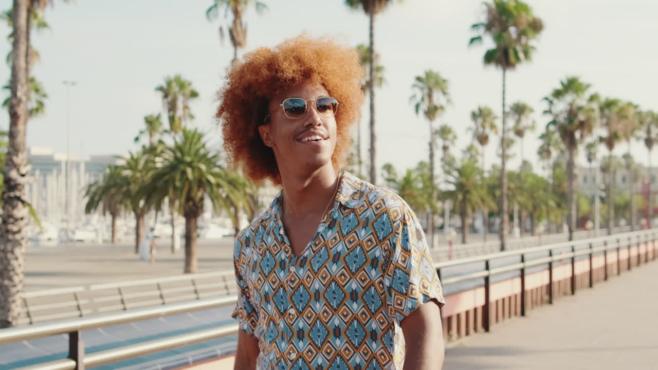 Smiling Young Man with Curly Hair Walking on Sunny Promenade