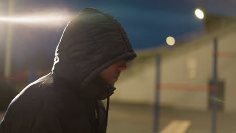 close-up side view of a person wearing a hooded jacket with bright light reflecting on him and the surroundings, with blur wall view