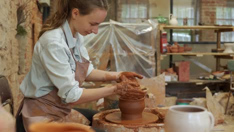 woman potter working on potter wheel making a clay pot. master forming the clay with her hands creating pot in a workshop