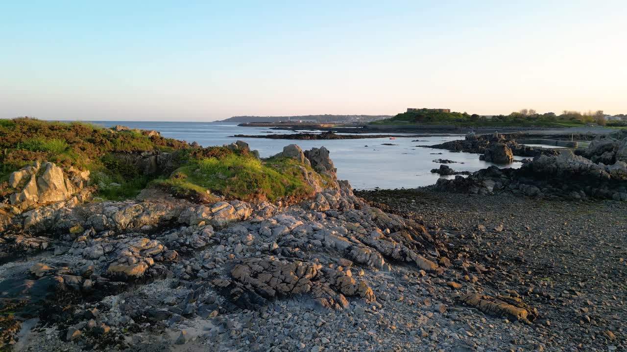 Lav flyvning over stenstrand og forstrand ved Bordeaux Guernsey ved lavvande med roligt hav på en lys sen eftermiddag
