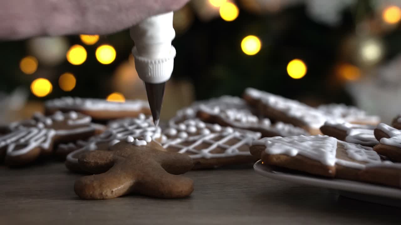 chef masculino decorando al hombre de pan de jengibre con glaseado de azúcar blanco con árbol de navidad en el fondo