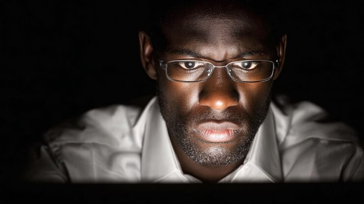 Un individuo concentrato impegnato nel lavoro al computer, illuminato dalla luce dello schermo, che mostra concentrazione e intento nel compito in un ambiente buio
