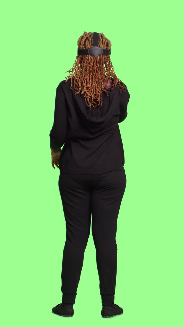 Vertical video: Young adult using vr glasses with full body over green screen backdrop