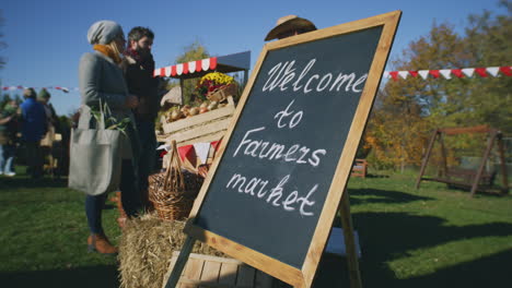 couple buy fruits and vegetables at farmers market couple buy fruits and vegetables at local farmers market woman contactless pays for purchases using smartphone autumn fair on weekend outdoors vegetarian and organic food agriculture