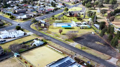 drone footage glides over coonabarabran, nsw, capturing suburban homes, roads, and a public swimming pool under bright daylight with steady, smooth camera movement