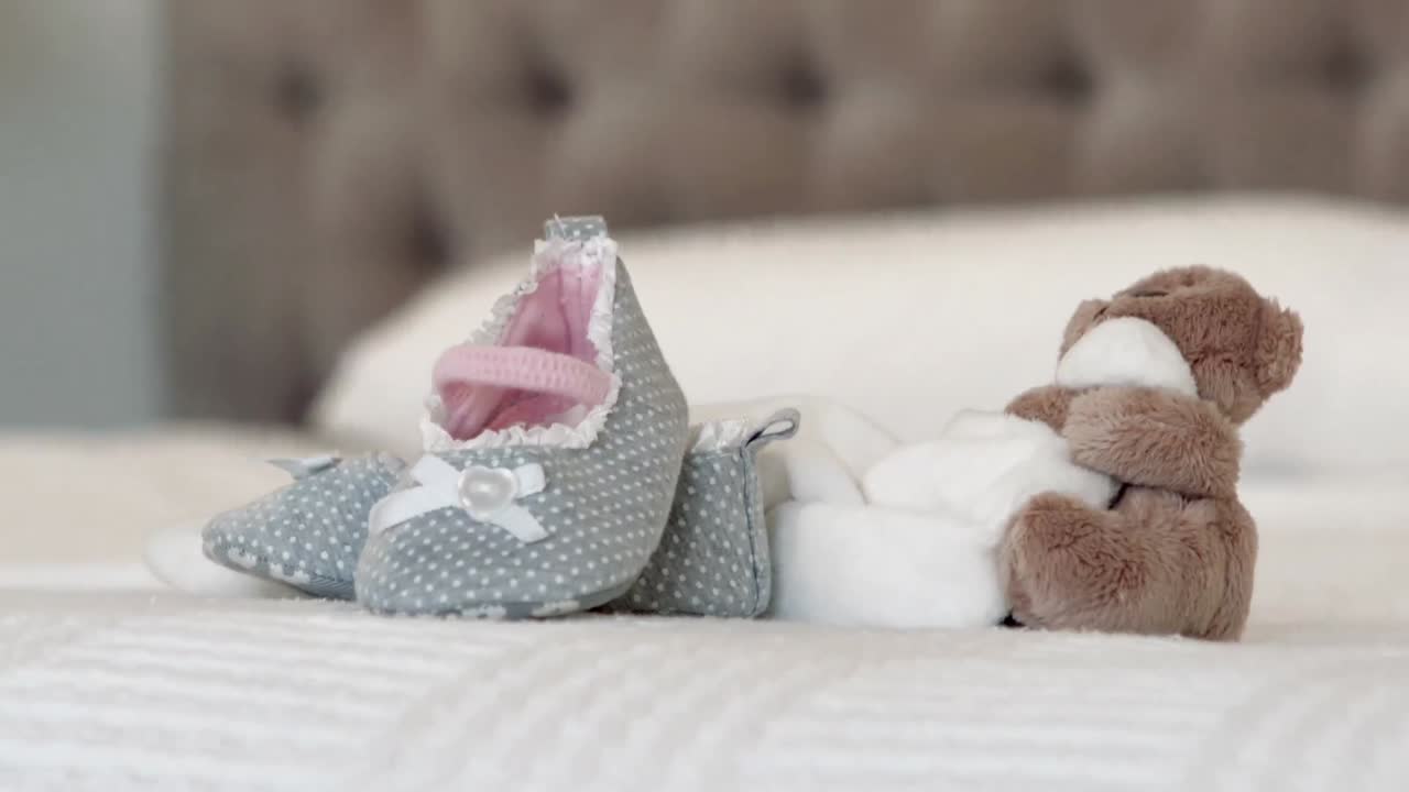 Baby shoes and teddy bear on bed