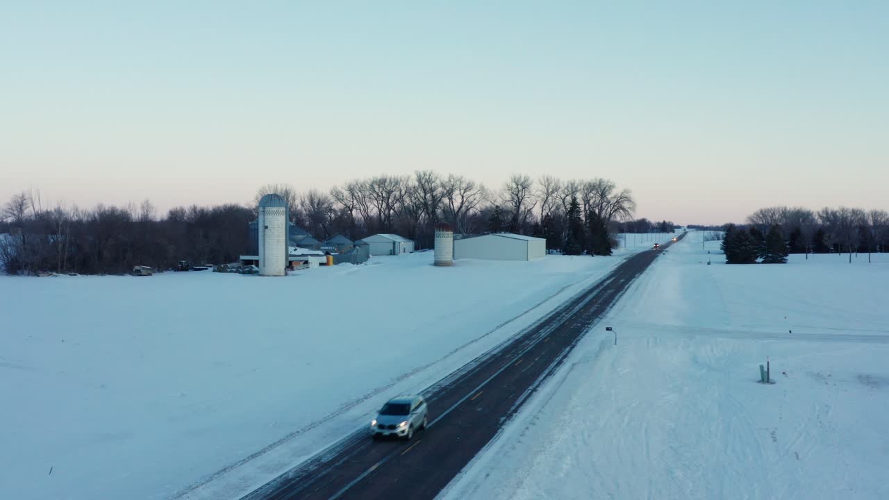 배경에 농장 실로와 함께 얼어붙은 시골 나라 도로를 내려가는 자동차의 높은 전망