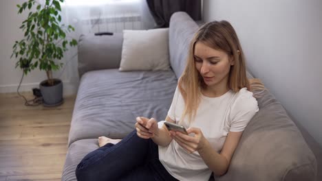 blonde woman sitting on a sofa, pays for purchases online with a credit card and phone home