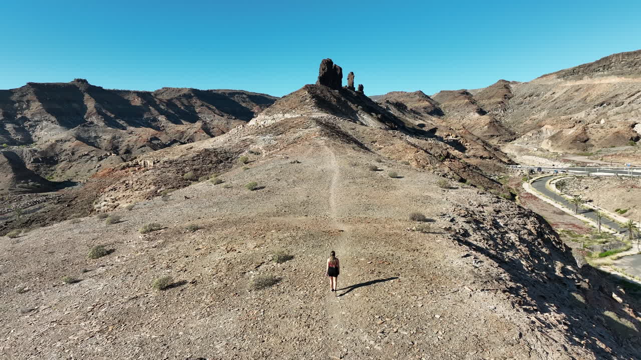 Giovane donna con i capelli lunghi cammina in direzione di una formazione rocciosa molto vicina alla spiaggia di Medio Almud, sull'isola di Gran Canaria, in una giornata di sole.