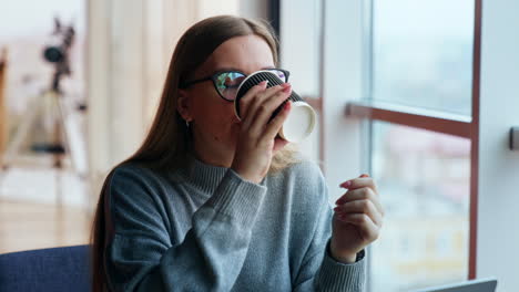 smiling dreamy lady drinks coffee looking into window. woman having a break from work at laptop. lunch time at the working place. close up.