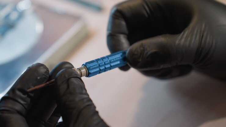 A close view of a technician's gloved hands adjusting a screw while working on a circuit board under a microscope