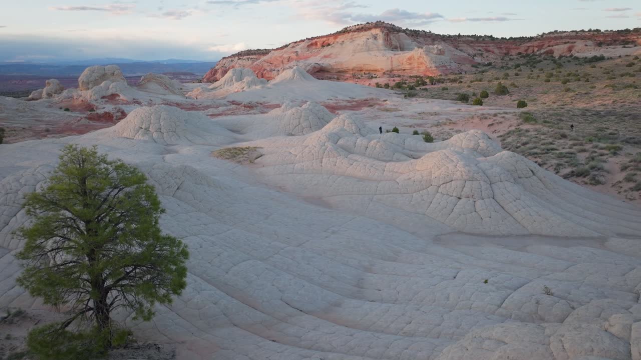 A drone slowly flying forwards through the unique sandstone features of White Pocket Arizona surrounded by the sandy desert of the Vermillion Cliffs