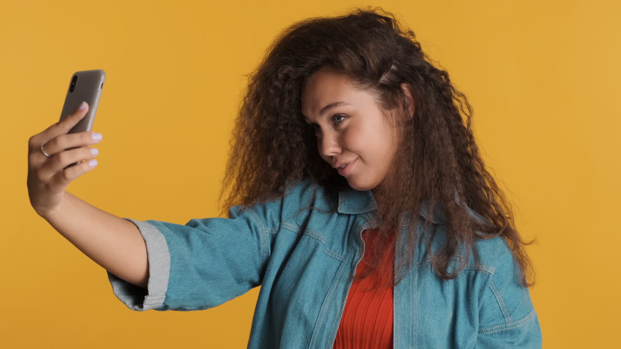 Caucasian curly haired woman taking selfies on smartphone.