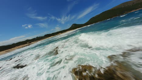 FPV-Drohne-Surft-An-Einem-Schönen-Tag-über-Atemberaubende-Brandungswasserwellen-Mit-Klarem,-Blauem-Wasser