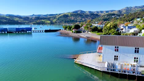 aerial footage of akaroa, showcasing vibrant waters, coastal buildings, and lush hills under clear skies
