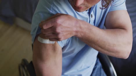 sección media de un hombre discapacitado caucásico en silla de ruedas que muestra un vendaje en el brazo después de la vacunación contra la covid