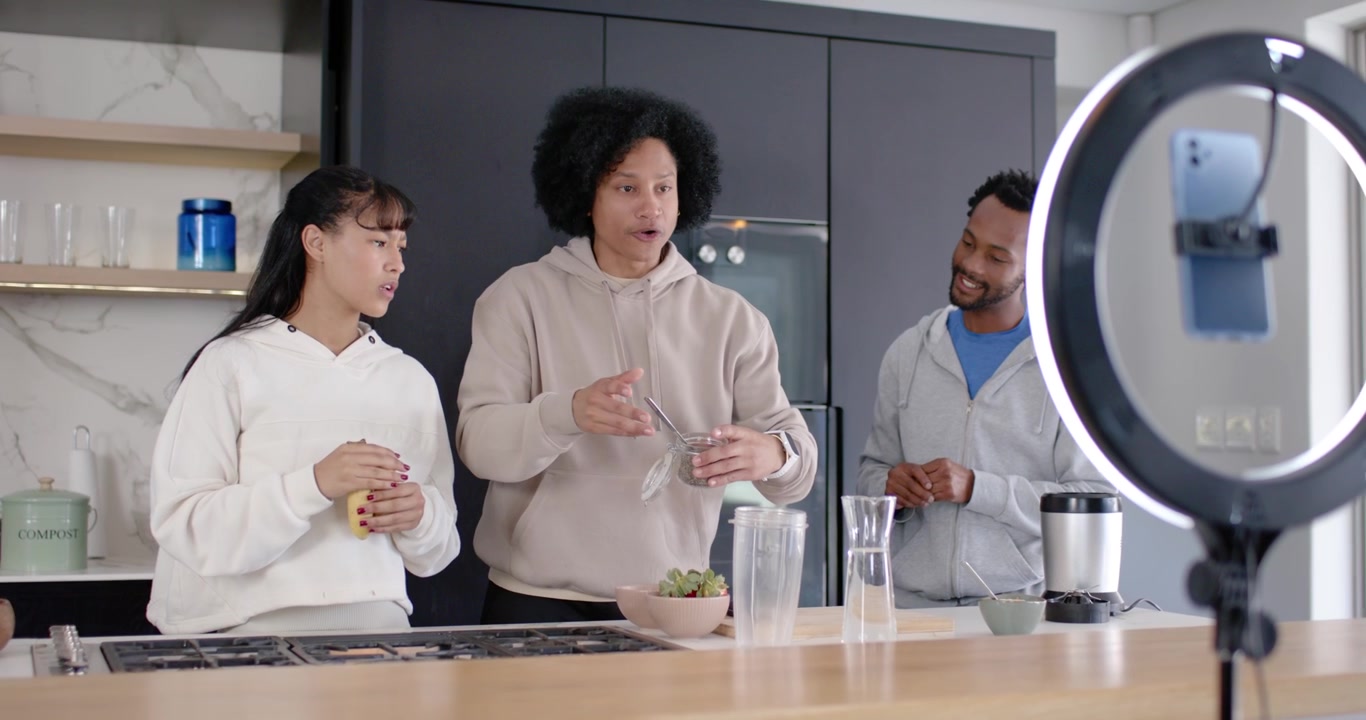 Trio africano al centro dell'isola della cucina che si protende per la brocca versando in una tazza, filmando con ring light