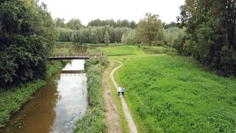 Drohnenansicht-Der-Aktivitäten-Im-Park:-Ein-Paar-Beim-Spazierengehen,-Menschen,-Die-Mit-Ihrem-Hund-Spazieren-Gehen-Und-Mehr-Am-Kanal