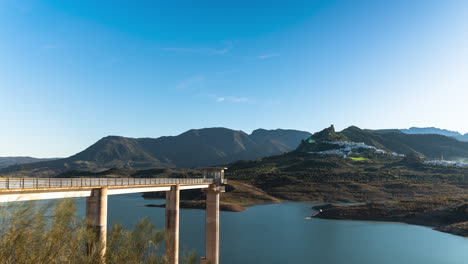 timelapse, zahara-el gastor reservoir in spain. small castle village is in the distance. beautiful blue skies, calm lake.