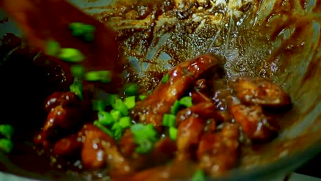 chicken wings sizzling in a pan with green onion over a hot stove, static shot