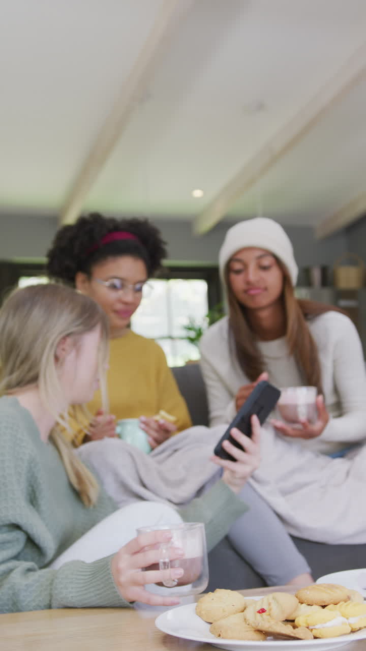 Vertical video of happy diverse teenager girls using smartphone at home, slow motion