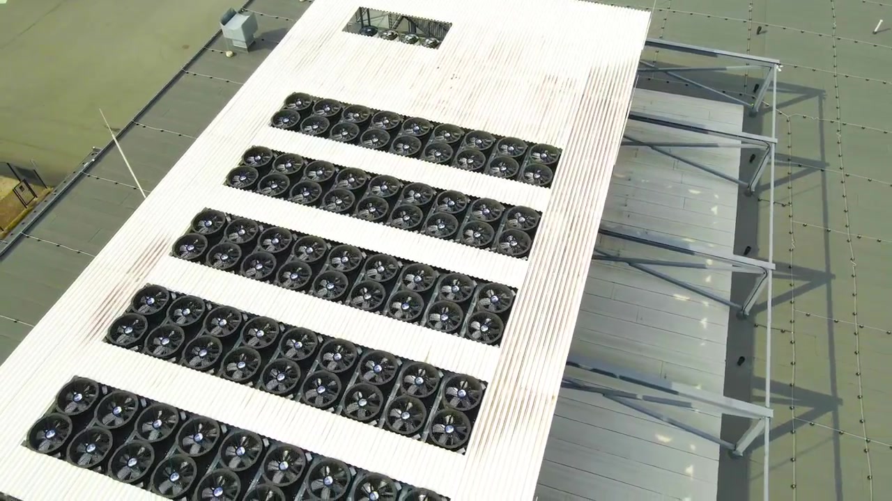 Industrial fans of a data center cooling system spinning on the rooftop of a large building, dissipating heat generated by servers to maintain optimal temperature for hardware operation