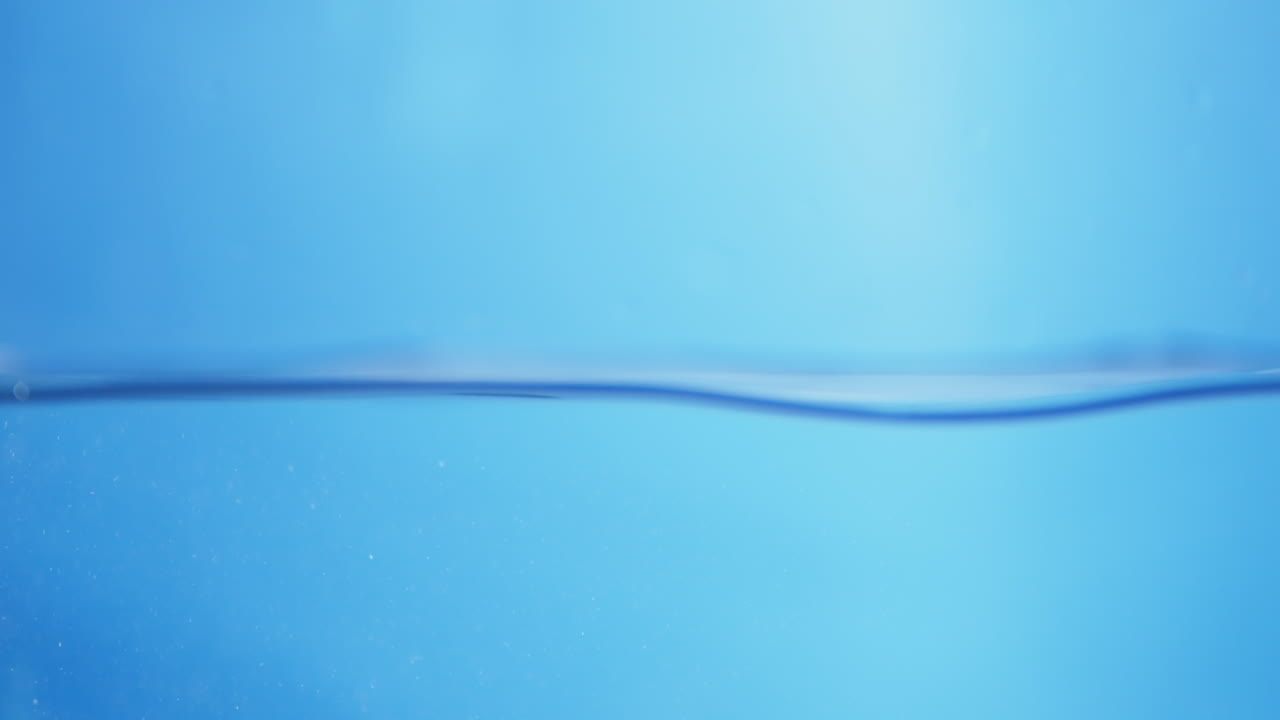 Water droplets fall from above, creating smooth circular ripples on the surface, representing purity, health, and refreshing clean liquid.