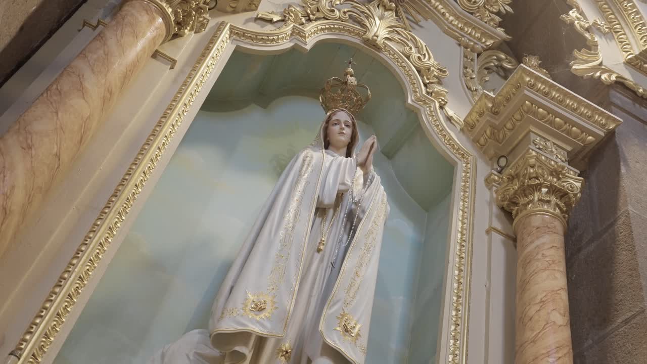 Vista dal basso della statua della Vergine Maria incoronata all'interno di una nicchia decorativa dell'altare con colonna a cornice dorata e sfondo cielo dipinto in una chiesa cattolica.